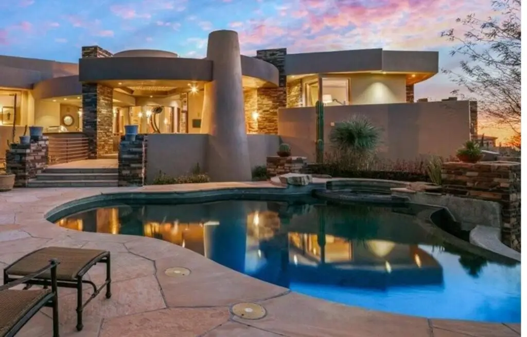 Contemporary desert home with curved pool and sunset lighting.