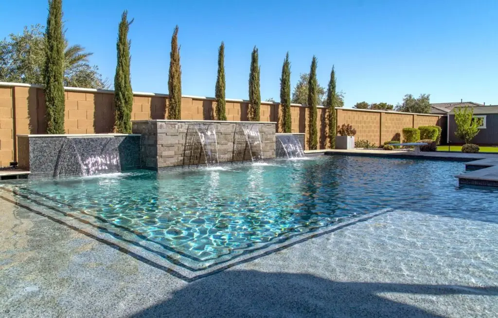 Modern pool with triple waterfall feature and tall evergreens.