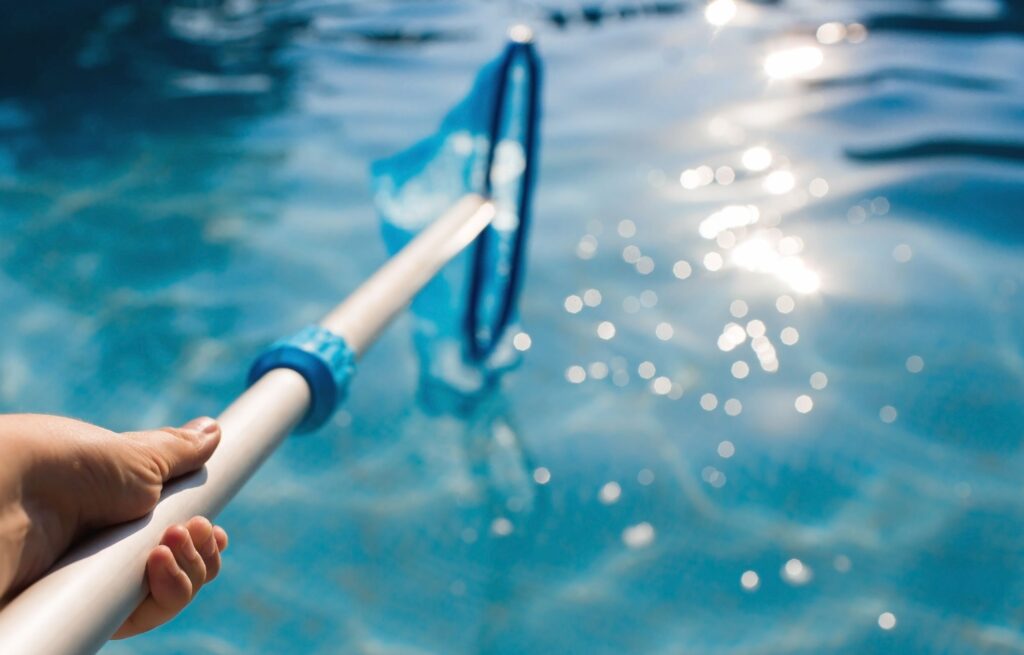 Pool cleaning skimmer in clear blue water under sunlight.